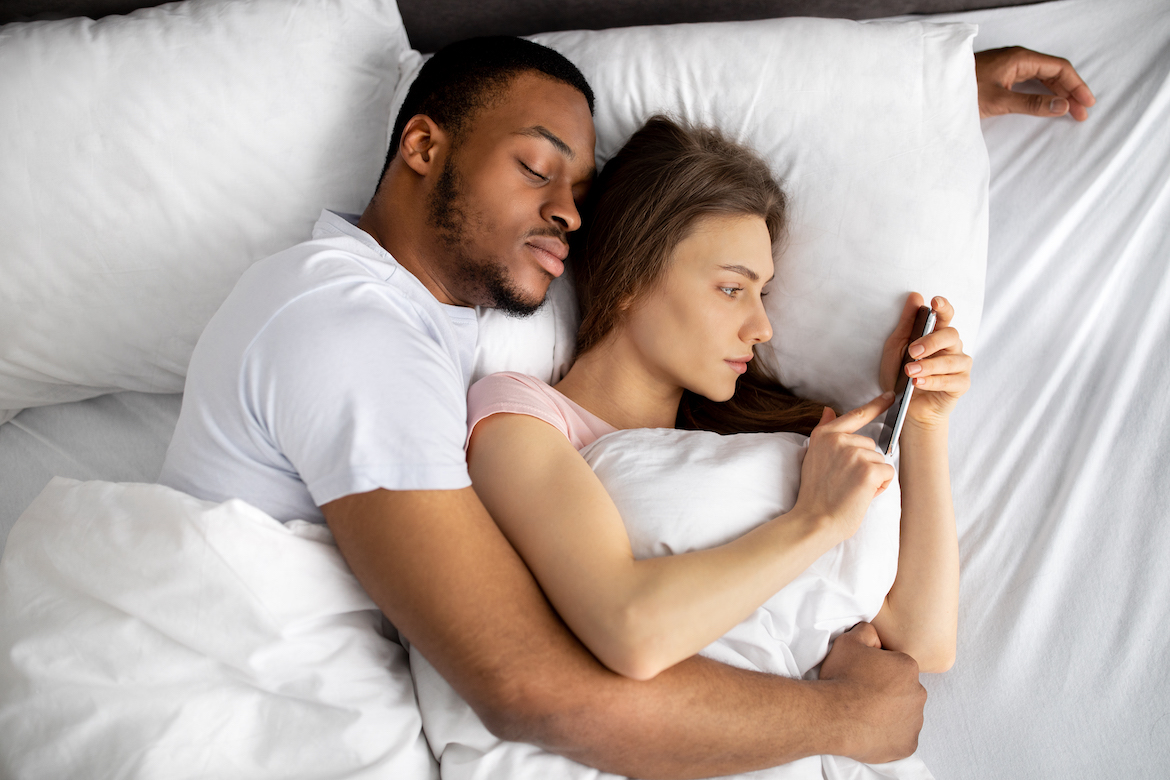 couple cuddling in bed with woman looking at her phone