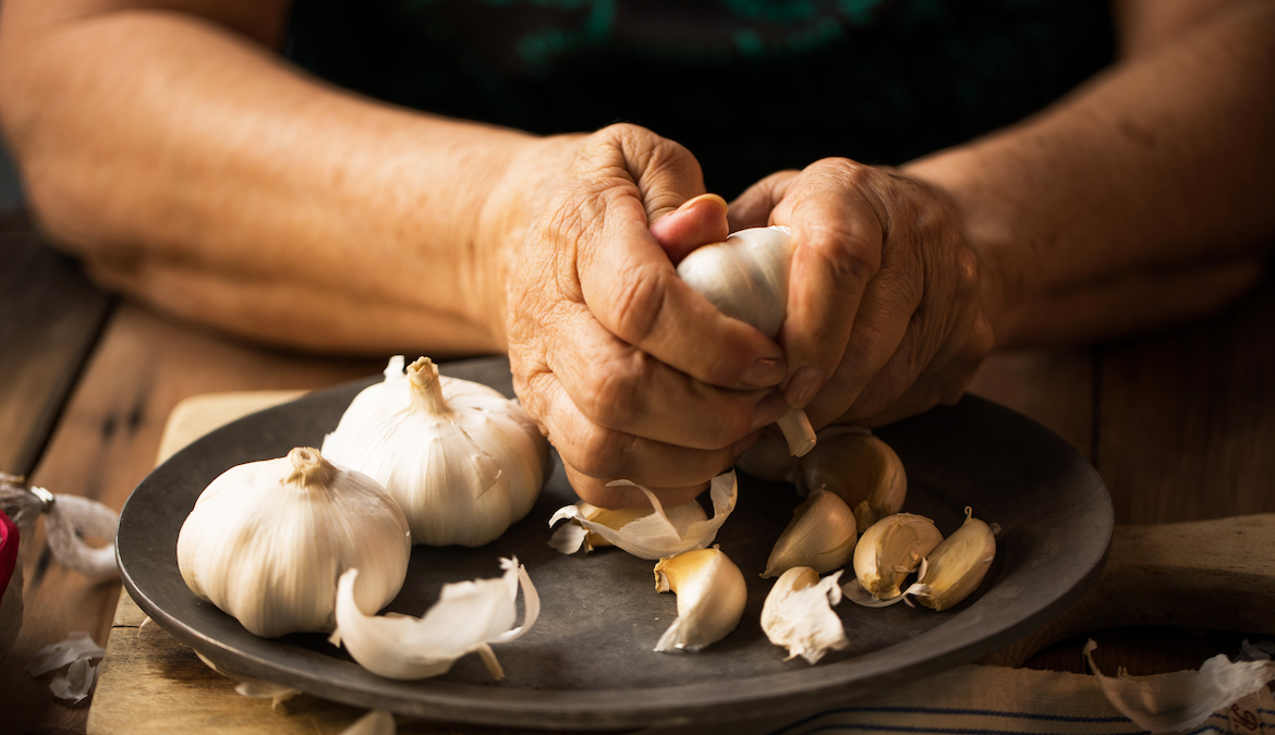 A woman prepares whole heads of raw garlic using her hands.