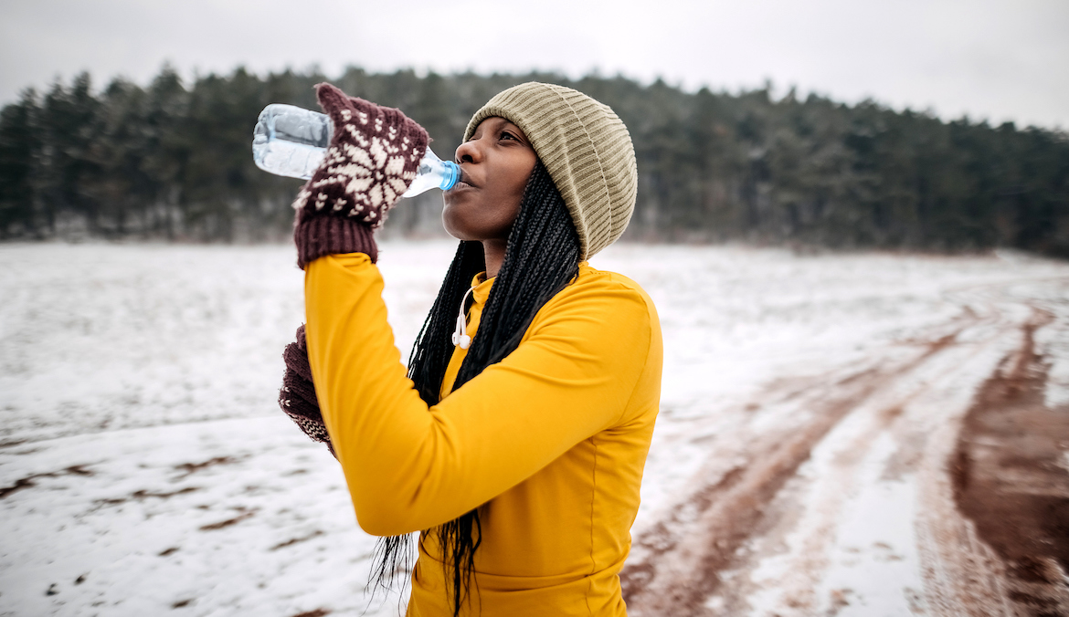 Female athlete in winter clothes drinking water before training on snow for
