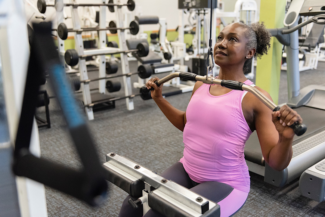 Older Black woman using weight machine at the gym.