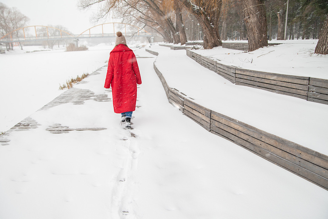 Woman walking in snow wearing red winter coat.