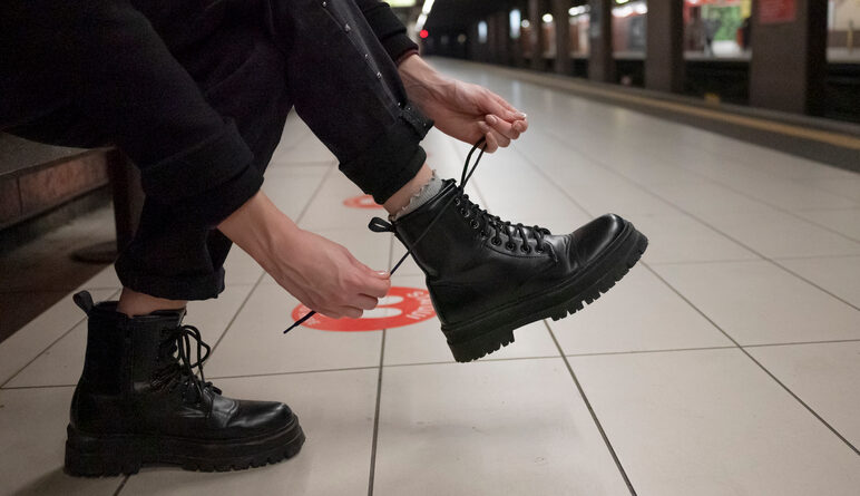 A close up photo of a person tying their boots while sitting at a subway station.