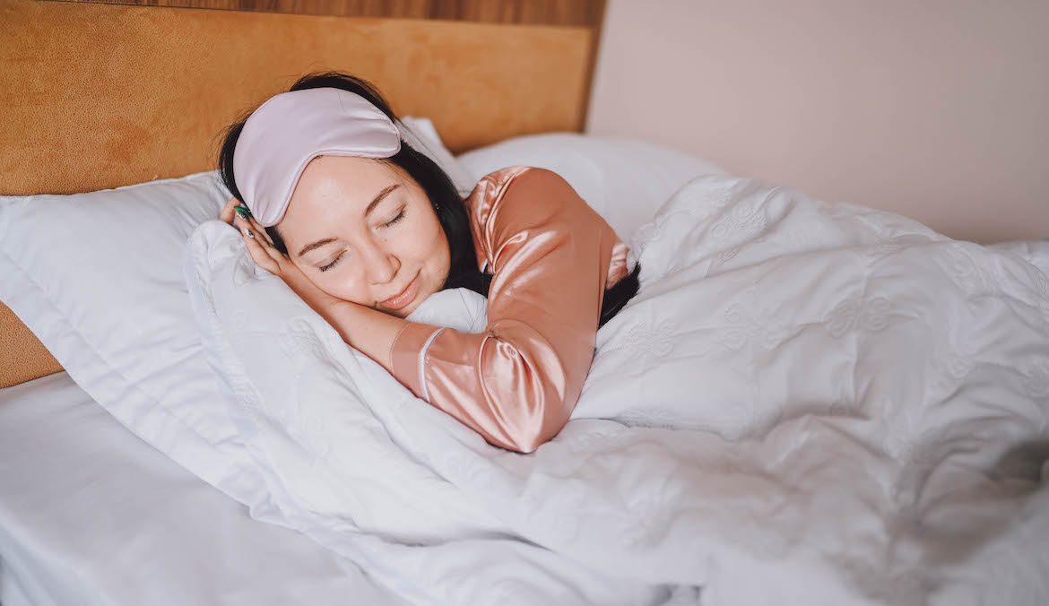 woman sleeping on a silk pillowcase wearing silk pajamas and an eye mask