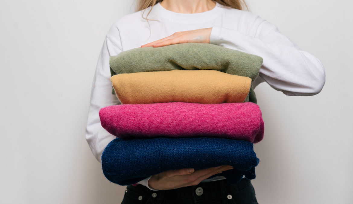 woman carrying stack of colorful cashmere sweaters
