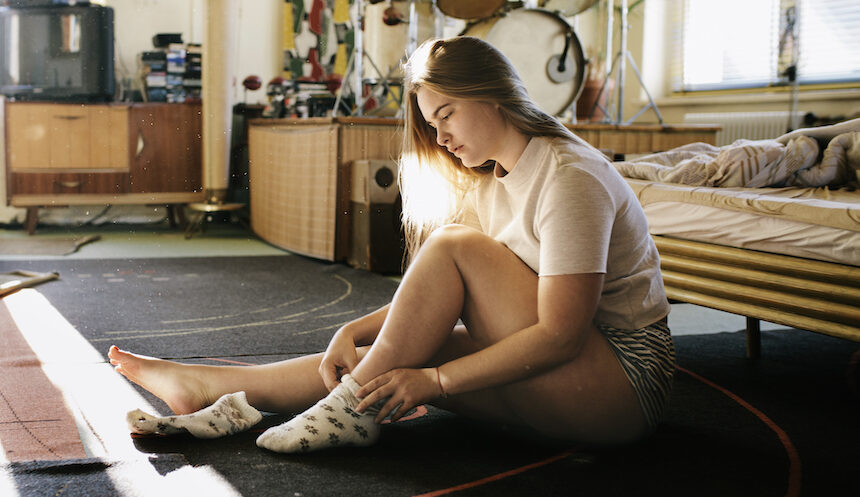 A young woman sits on her bedroom floor while switching out her socks.