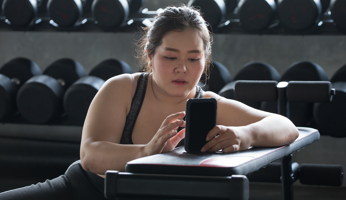 young asian woman using smartphone and relaxing in gym