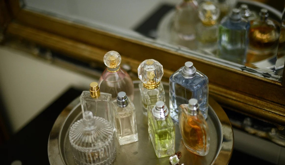 Perfume bottles displayed on a silver tray by an antique mirror.