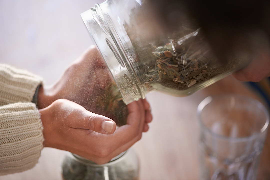 Woman transferring dried herbs from a big jar to a smaller one.