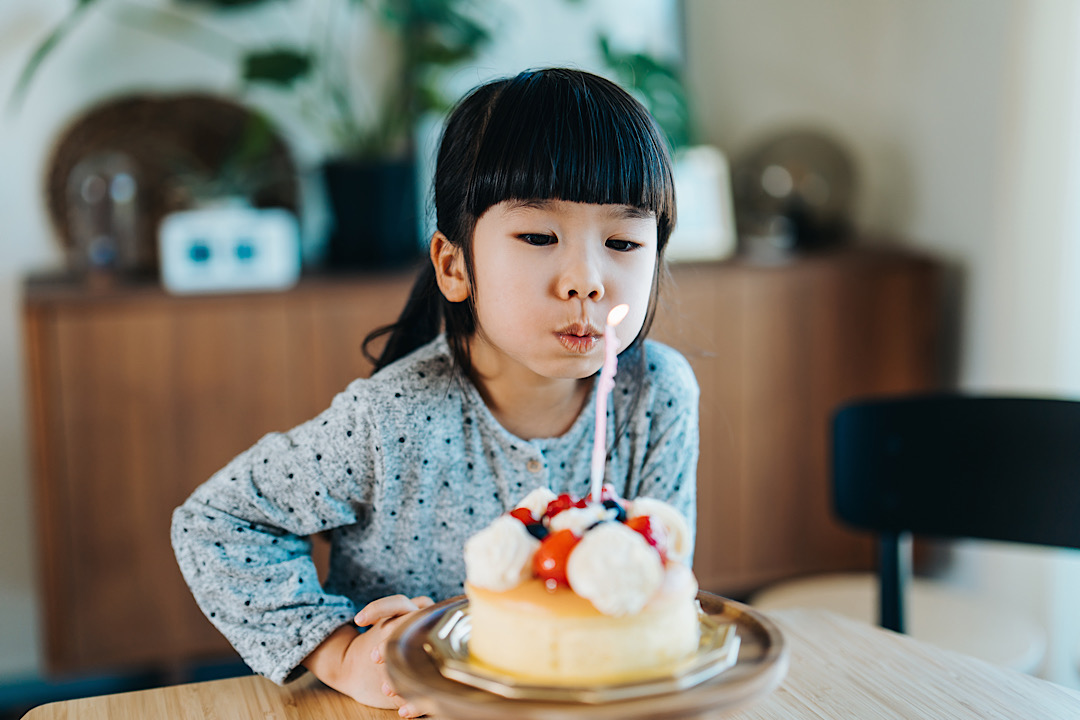 Young Asian girl blowing out a candle on her cake.