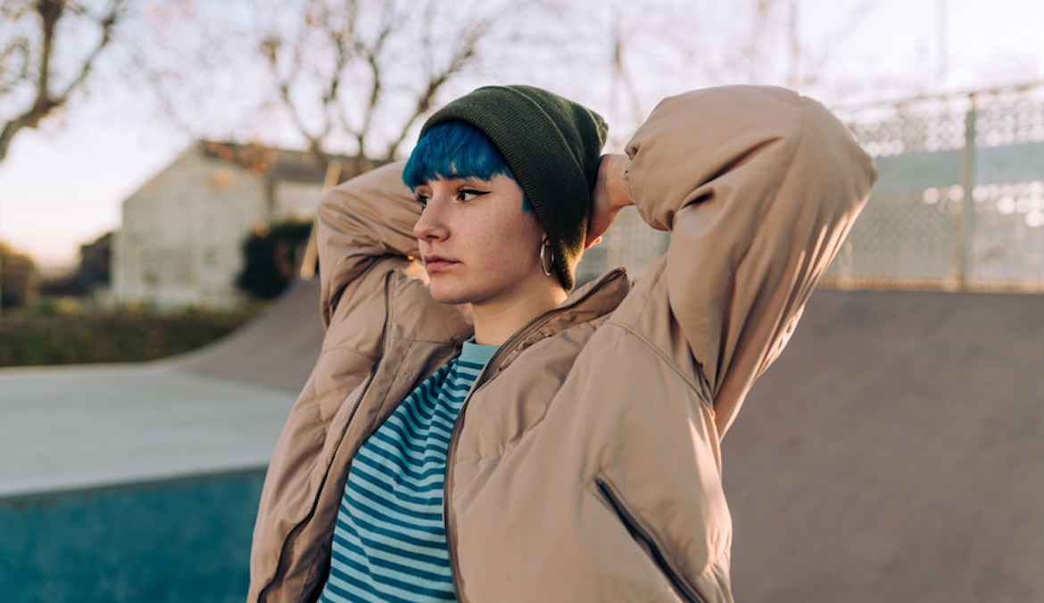 person with blue hair, wearing urban clothing, looking thoughtful and melancholic