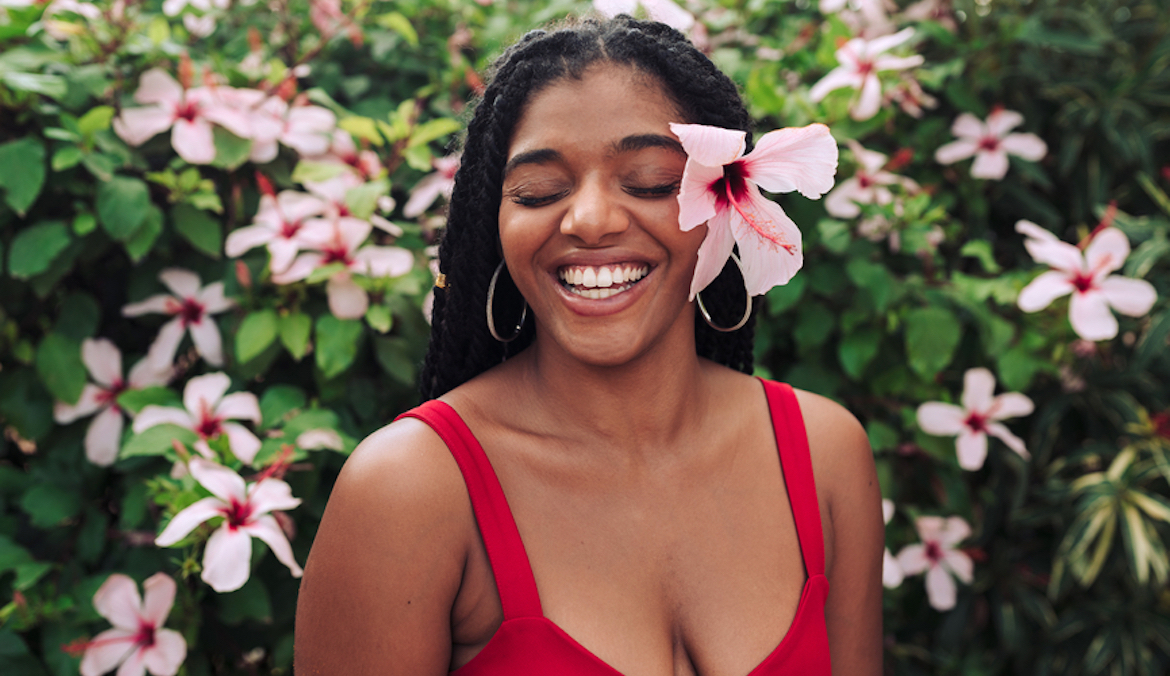 beautiful afro-descendant woman poses with a pink flower on her ear and smiles with her eyes closed