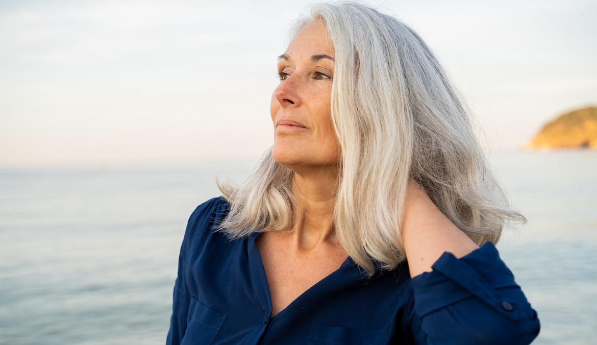 Portrait of Beautiful mature woman relaxing at beach during sunsrise looking away touching her hair
