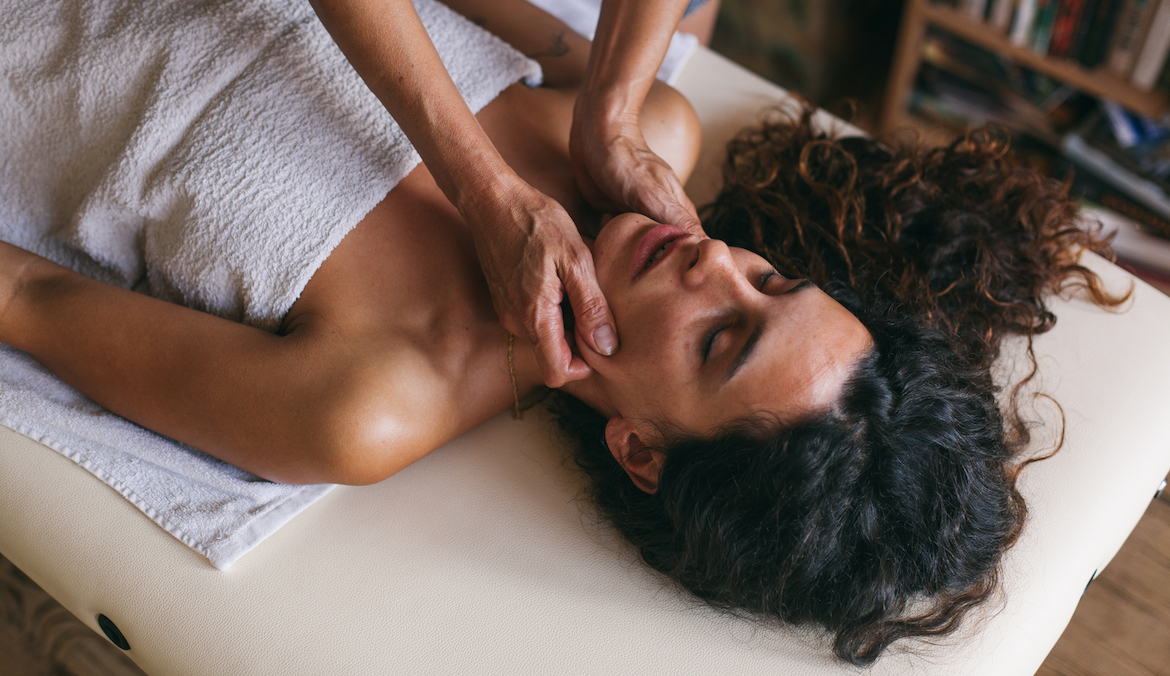 Female hands massaging face of brunette woman lying on a massage table.