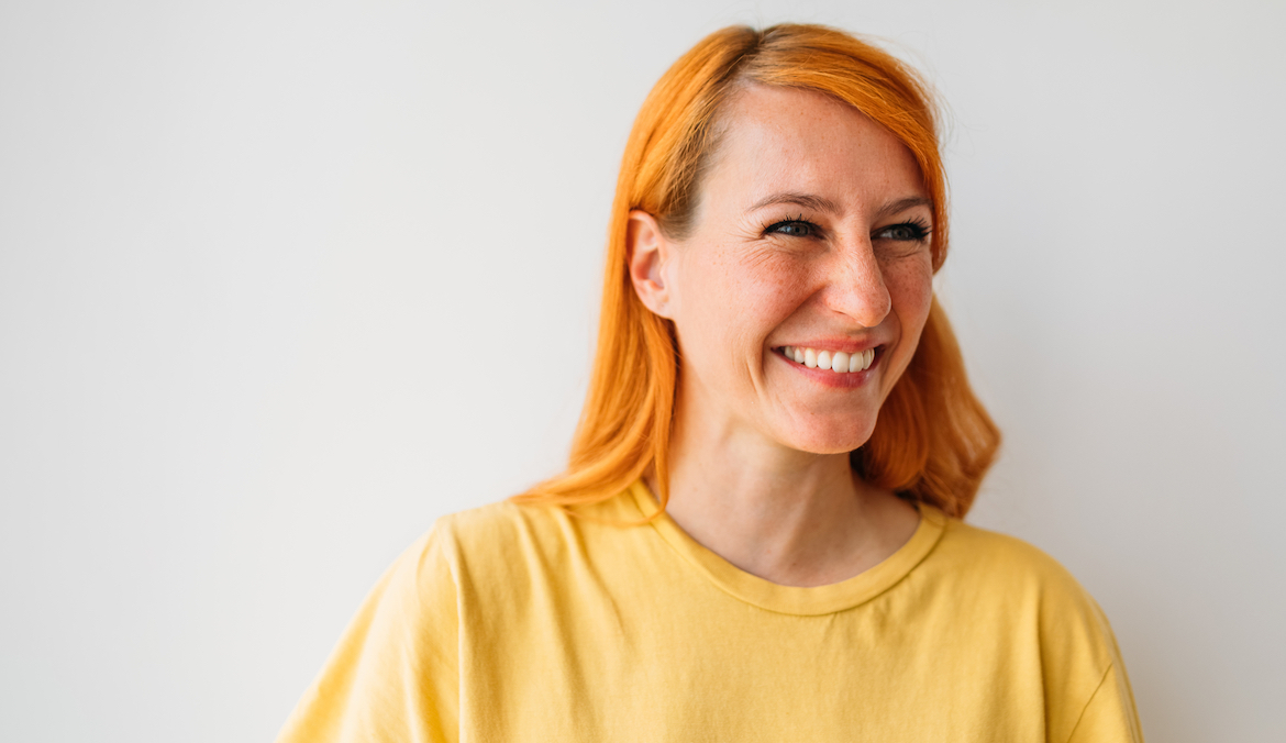 Portrait of beautiful redhead woman standing against white wall and smiling