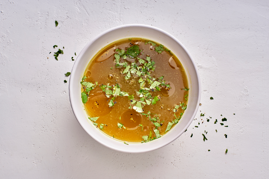 Bone broth in a bowl garnished with herbs.
