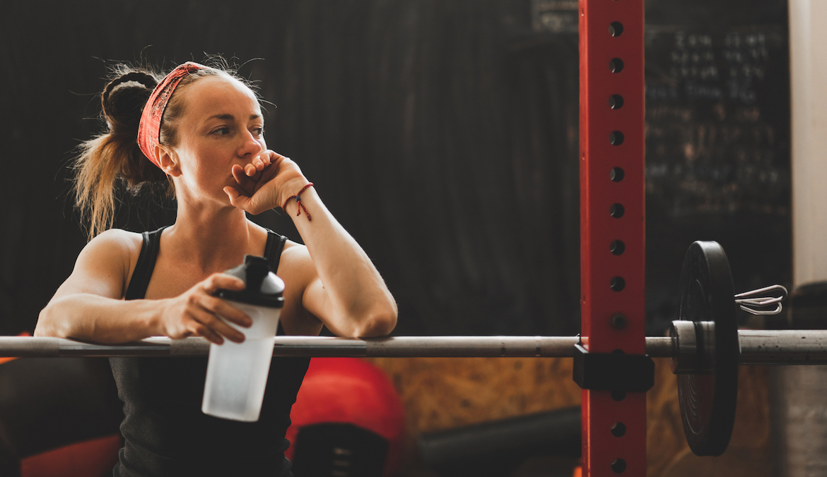 A woman looking into the distance at a squat rack who appears to be not in the mood to work out.