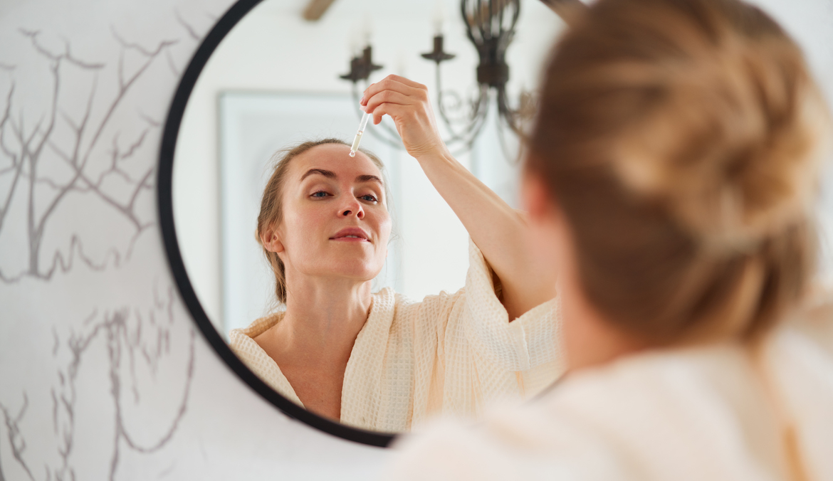 woman applying the three ships replenish serum to her face in front of the mirror