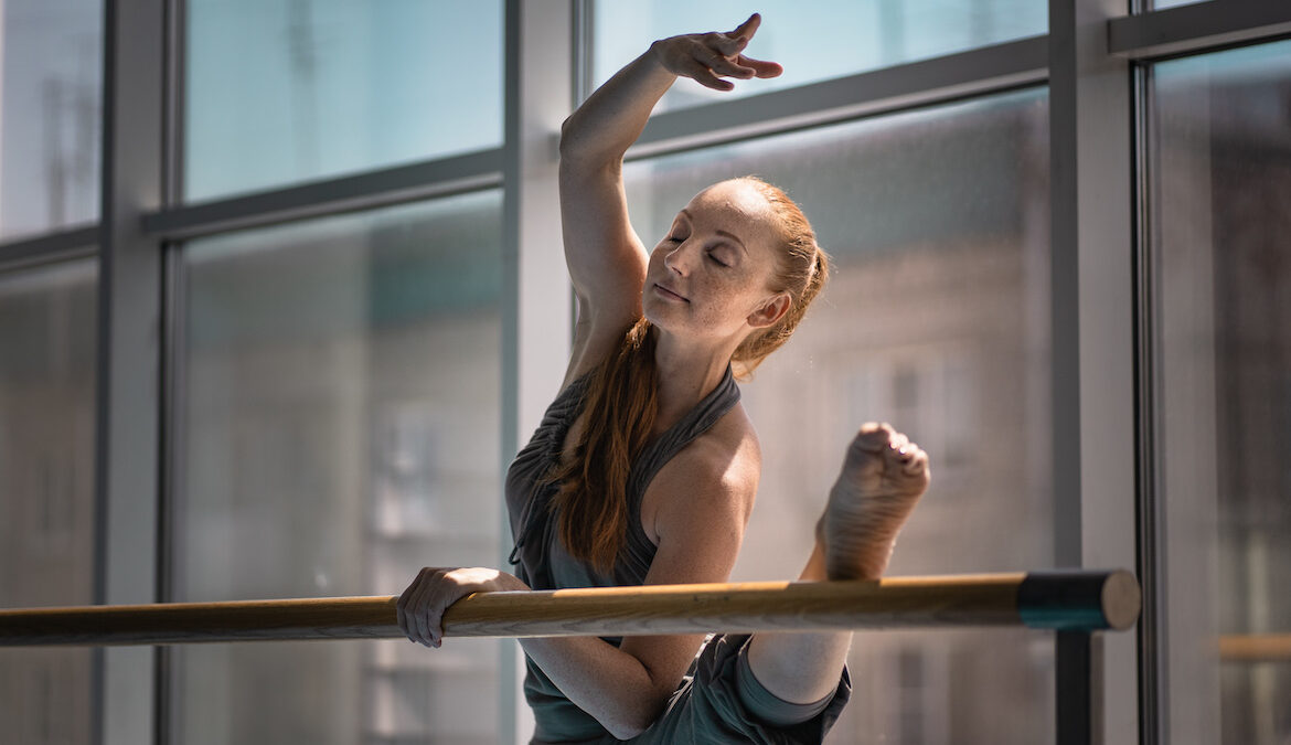 A young dancer stretches her leg on a barre during a workout routine.