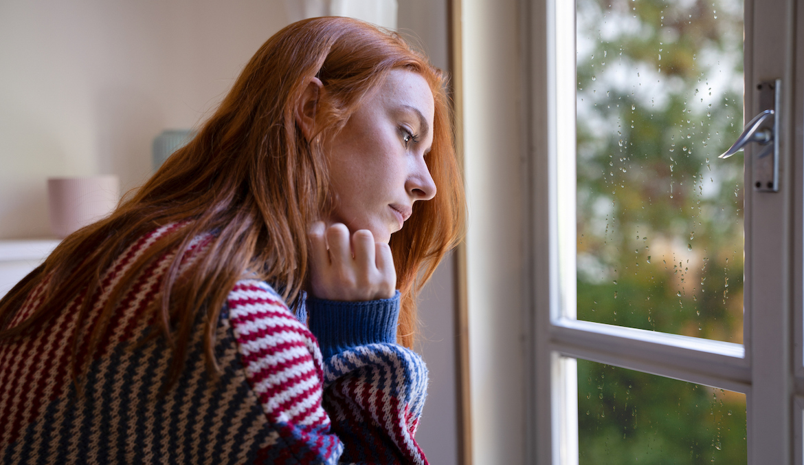 A young redheaded woman looks off into the distance out a window.