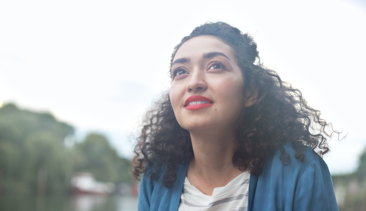 A young woman with curly hair looks into the distance and thinks.