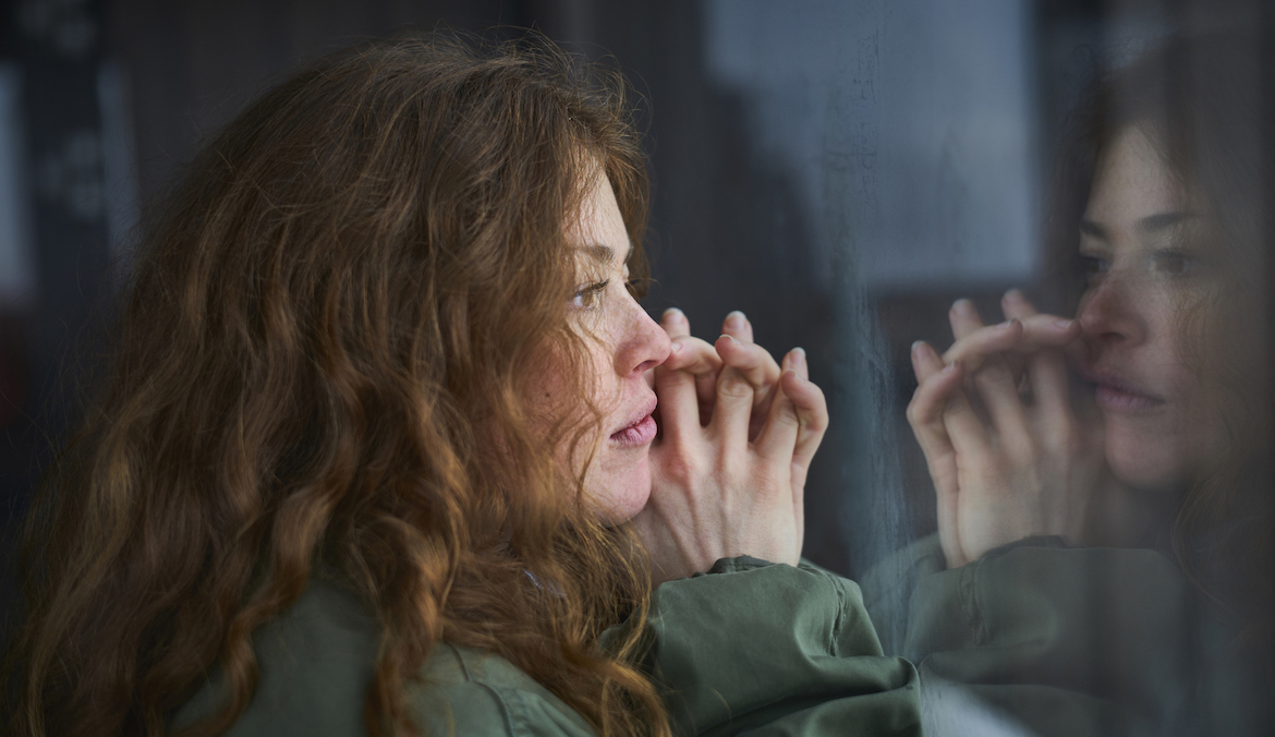 A young woman with curly red hair thinks and stares out a window.
