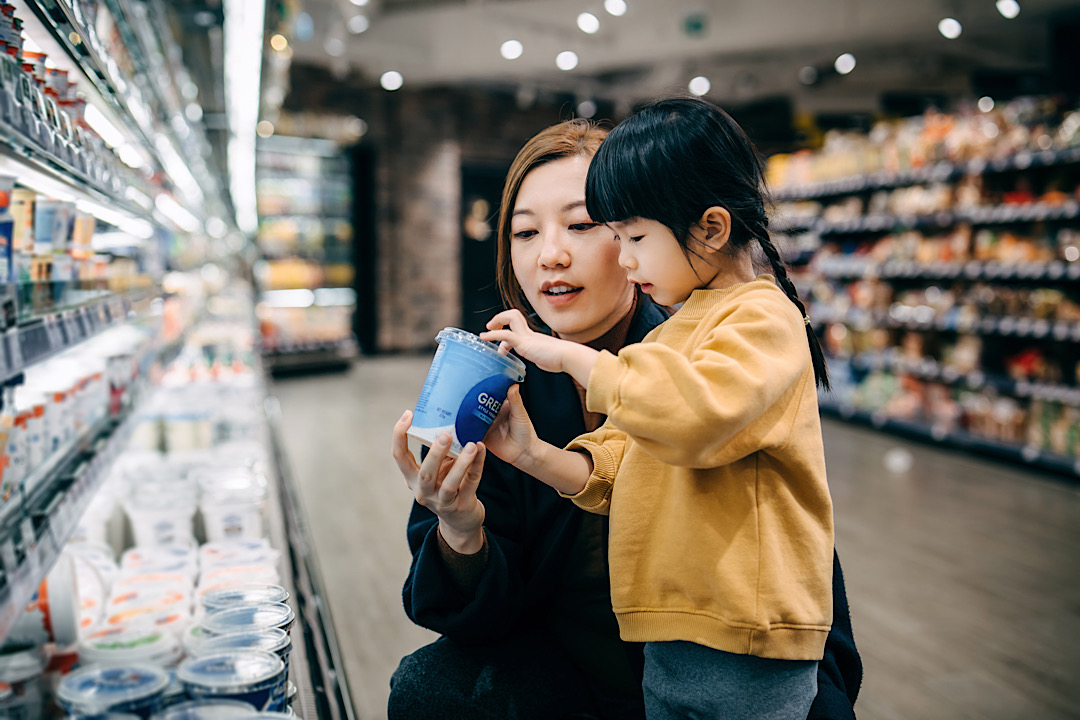 Mom and daughter looking at Greek yogurt container in grocery store