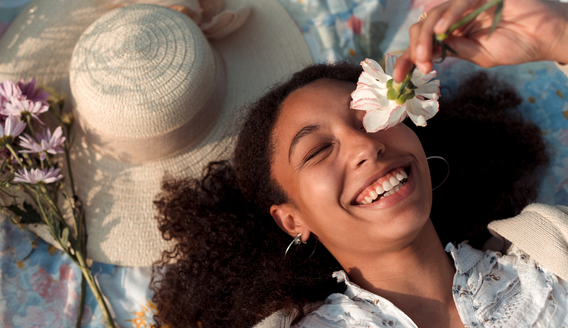Portrait of a cute young woman holding a white flower over her eye and laughing.