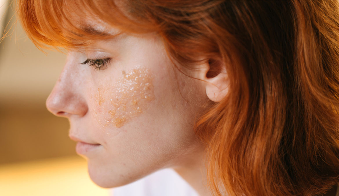 Young red hair woman doing skin care with sugar face scrub.