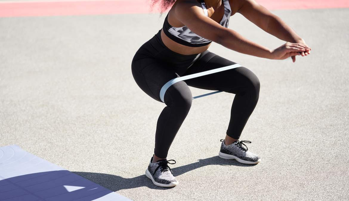 A woman in a squat with a resistance band around her thighs above her knees.