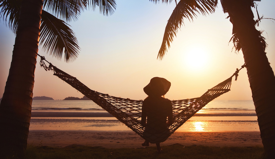 woman sitting in hammock under palm trees at sunset