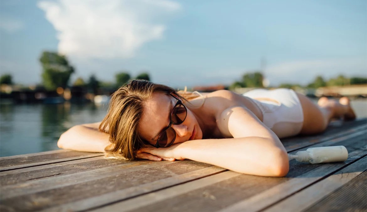 A woman laying in the sun with a bottle of sunscreen.