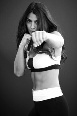 A woman showing a six pack with her arms in a boxing position by her face.