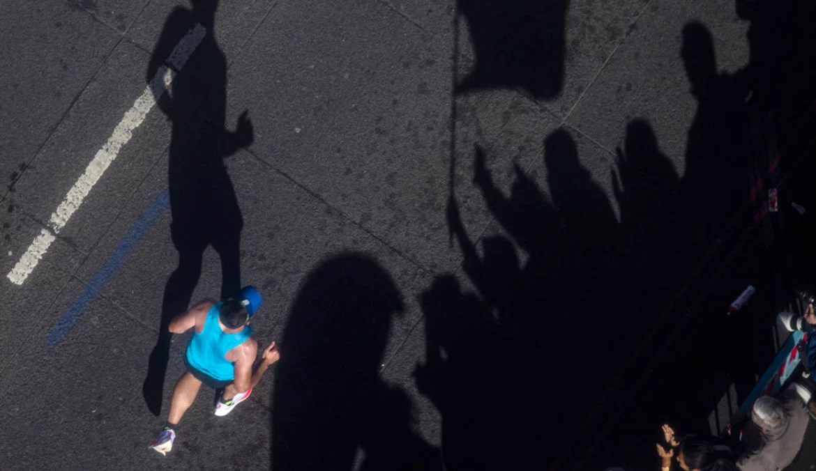 overhead shot of a runner in a race, next to shadows of a crowd with a flag