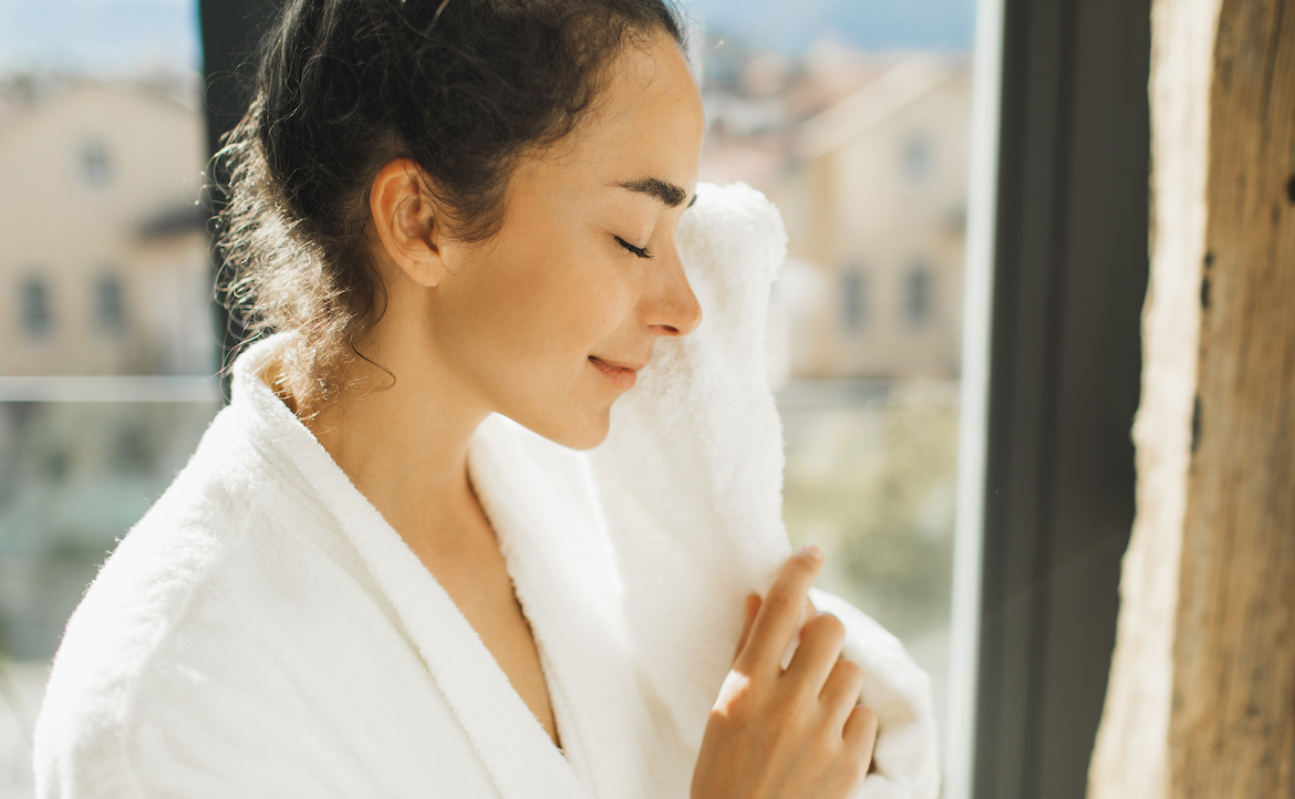 Woman drying her face with a white towel after washing with The Ordinary Glycolipid Cleanser
