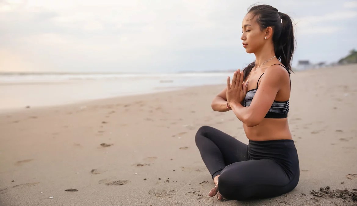 Close up shot of fit woman practicing meditation with hands on yoga prayer position, in empty beach