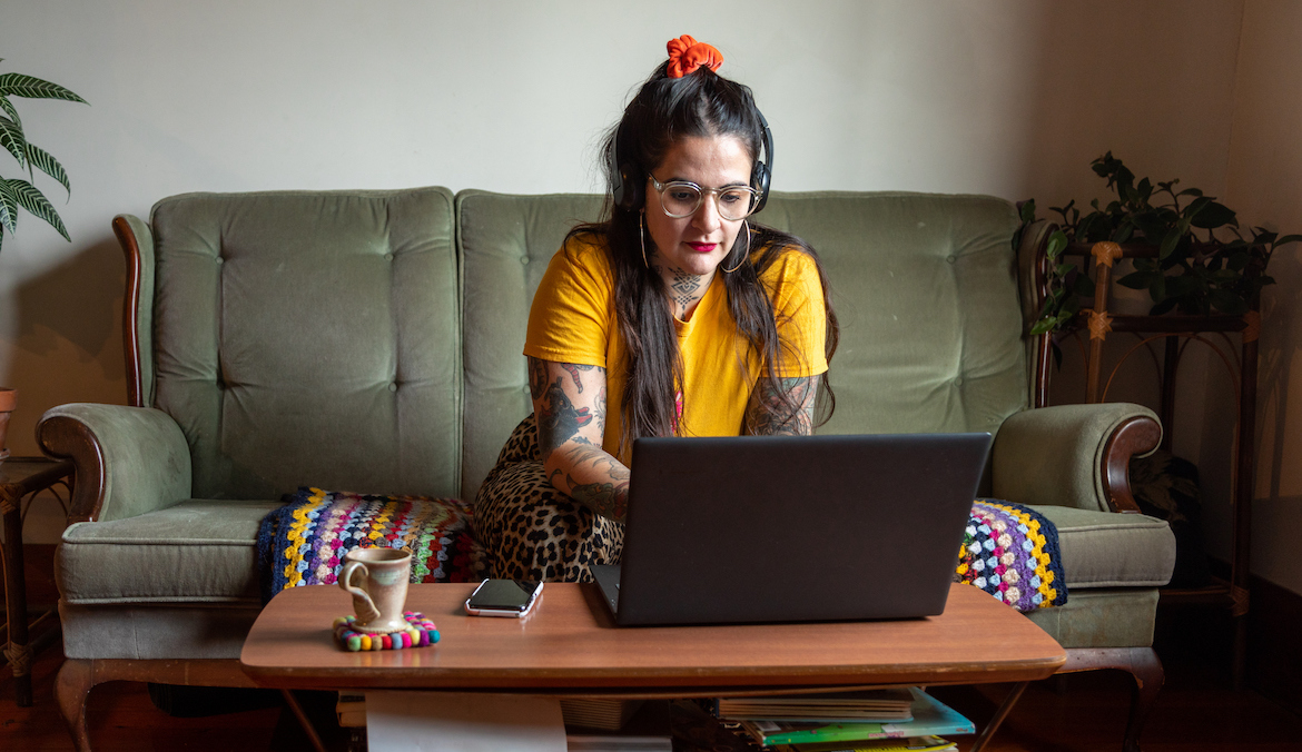 Tattooed woman on sofa working on laptop