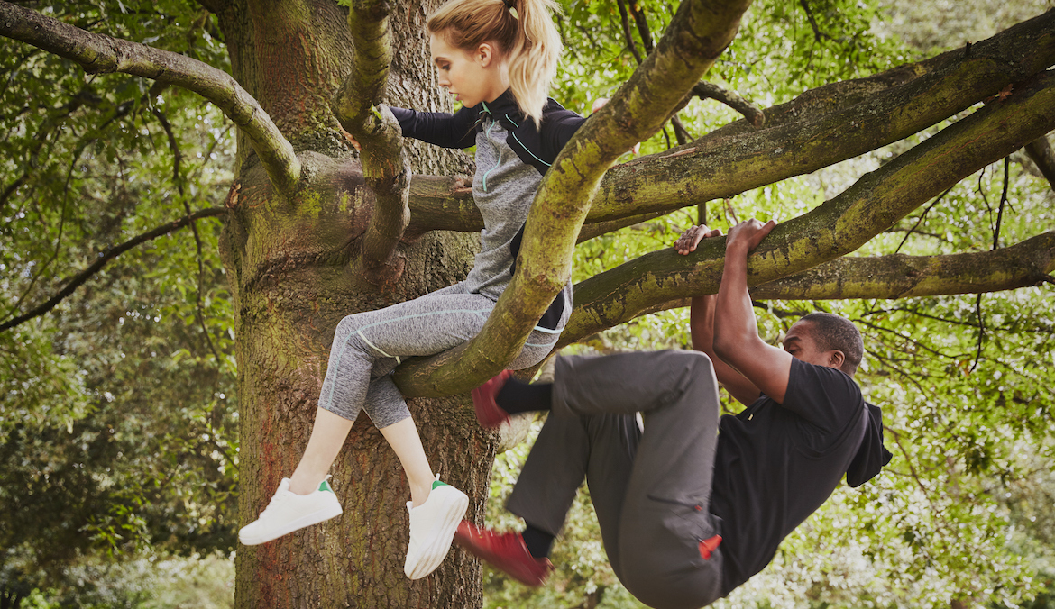 Personal trainer and young woman climbing up park tree