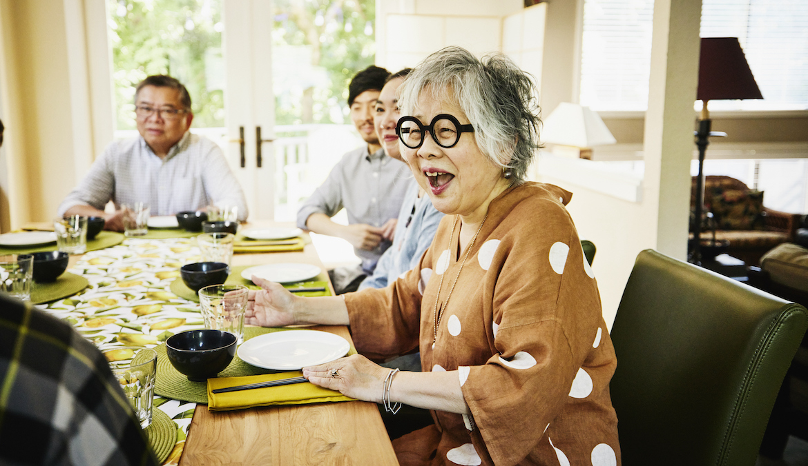 Medium wide shot of smiling grandmother seated at dining room table for multigenerational family dinner