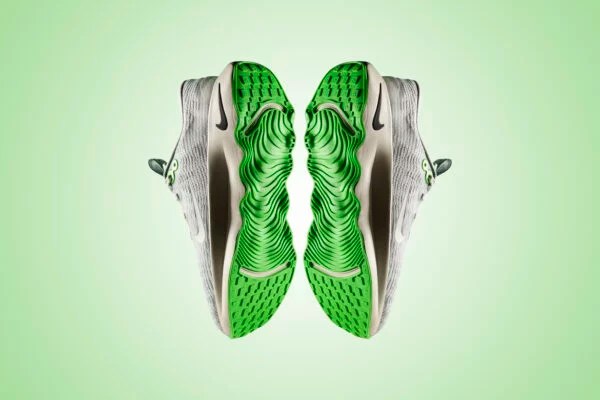 A pair of tennis shoes seen from the bottom, showing a neon green sole with lots of grooves.