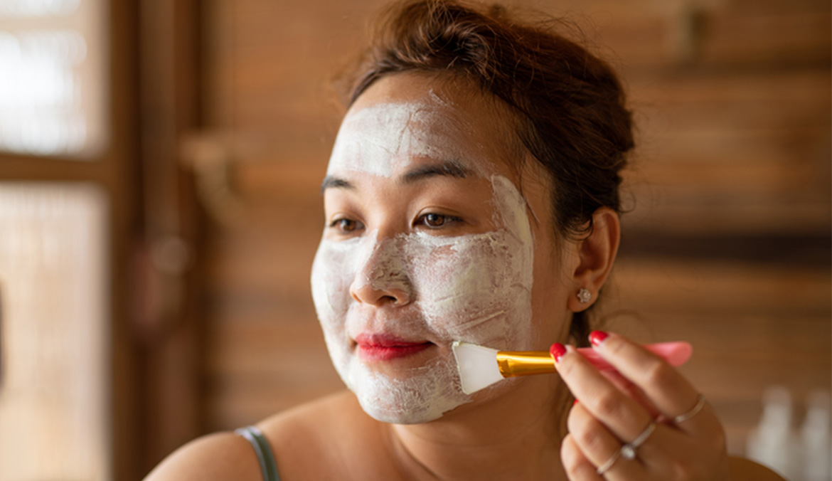 Young woman applying clay mask at home.