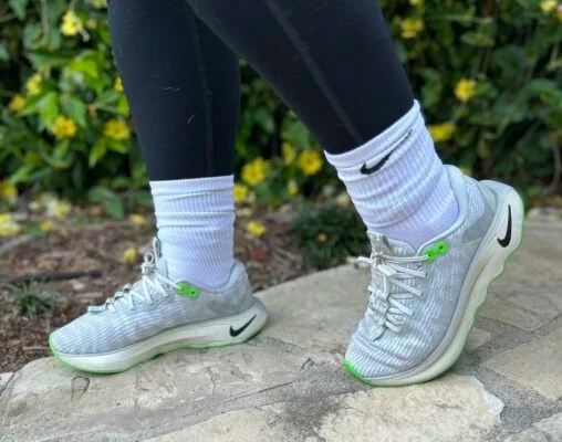 Gri, beyaz ve yeşil tenis ayakkabıları giyen bir kadının ayaklarının yakından görünümü.