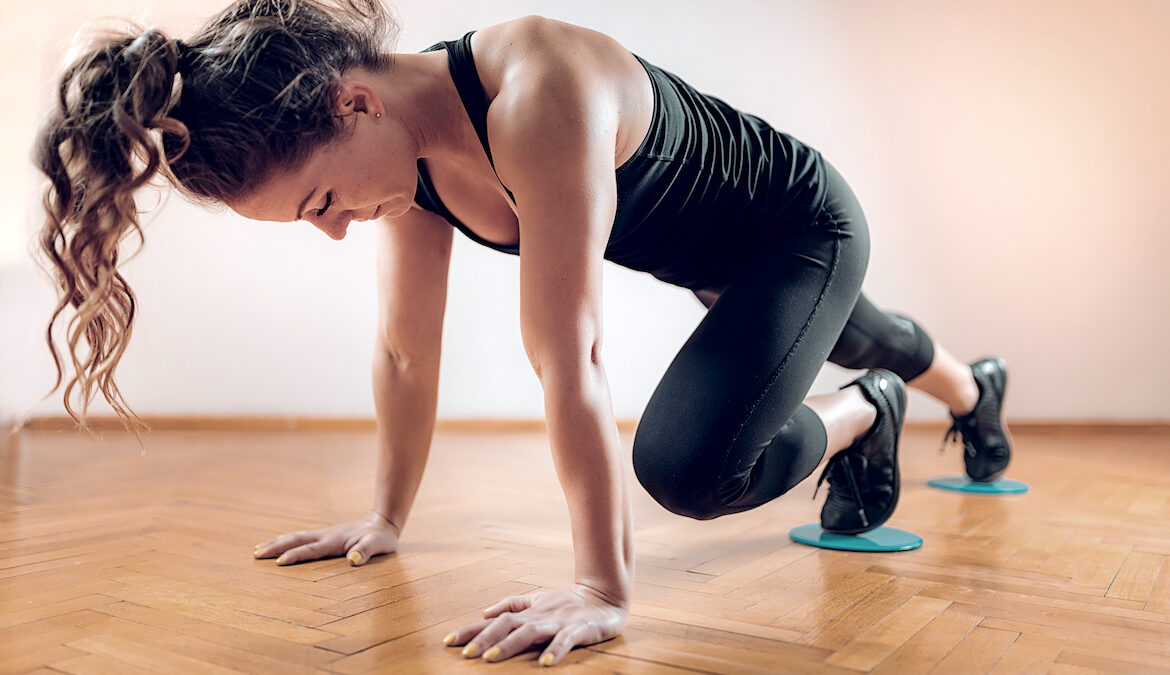 A young woman wearing athletic clothing performs mountain climbers while using workout sliders.