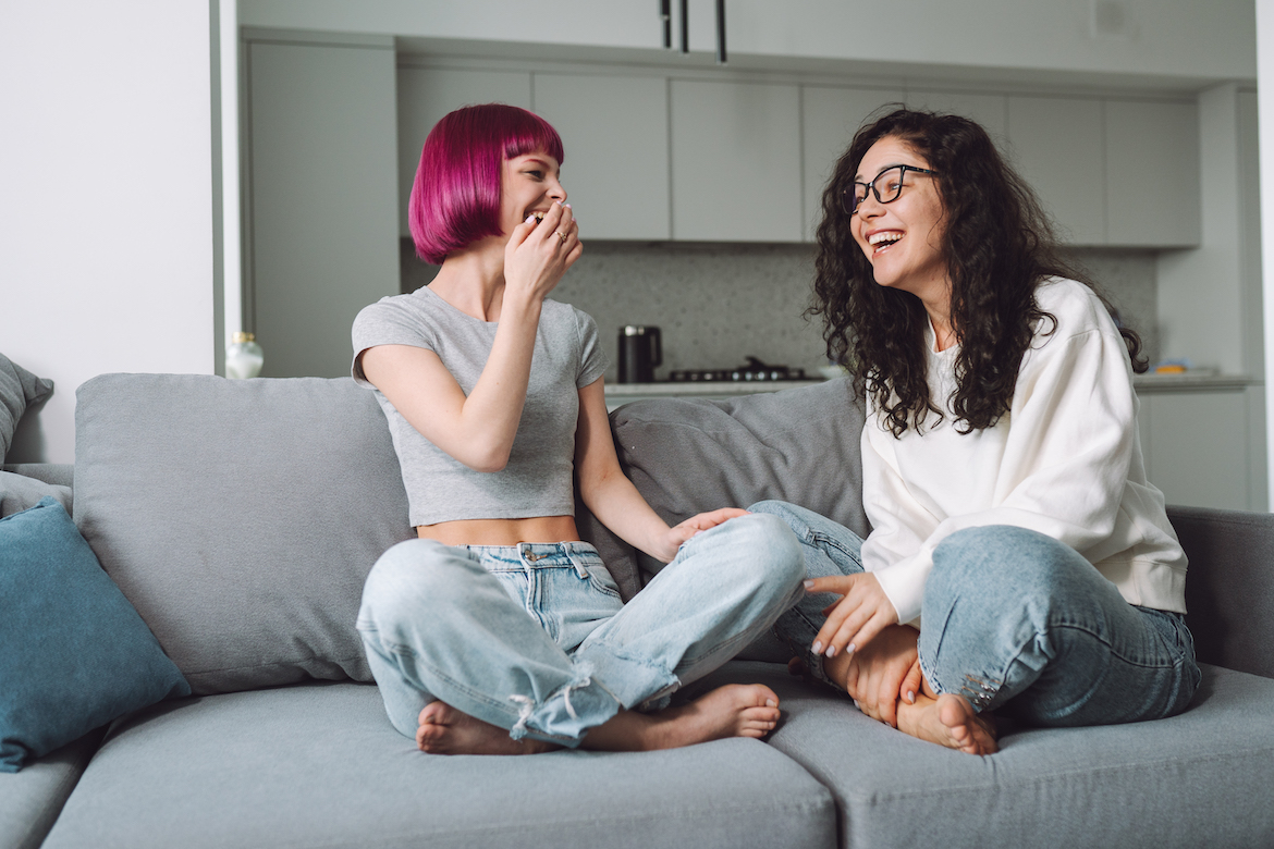 Laughing positive pink haired teen girl talking with adult woman in eyewear, sitting on a coach