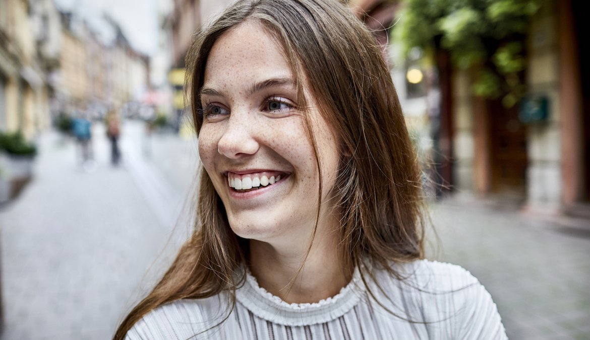 portrait of woman with long brown hair smiling while walking down the street