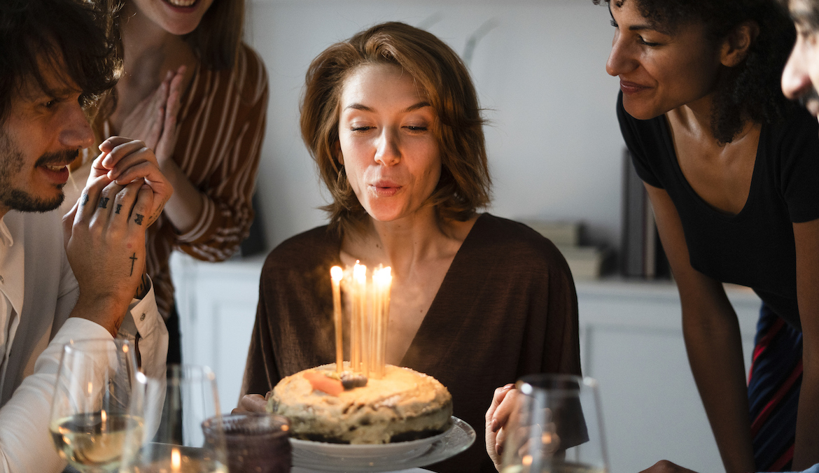 birthday blues woman blowing out birthday candles on cake surrounded by friends
