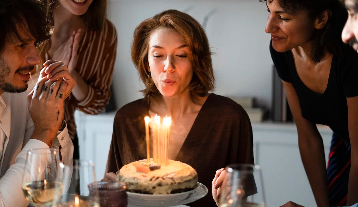 birthday blues woman blowing out birthday candles on cake surrounded by friends