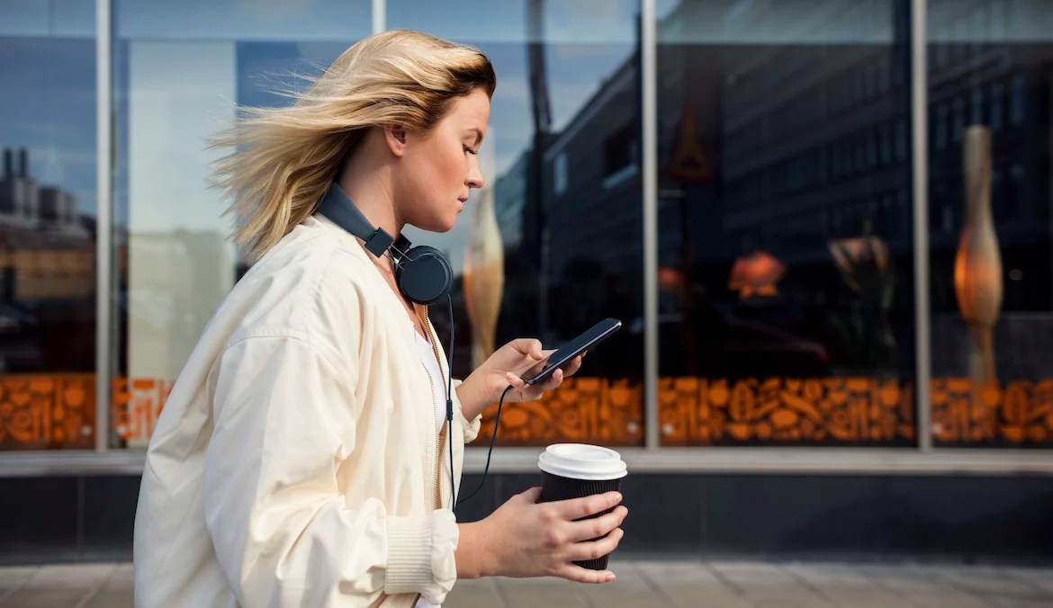Side view of woman using mobile phone while holding disposable cup against building