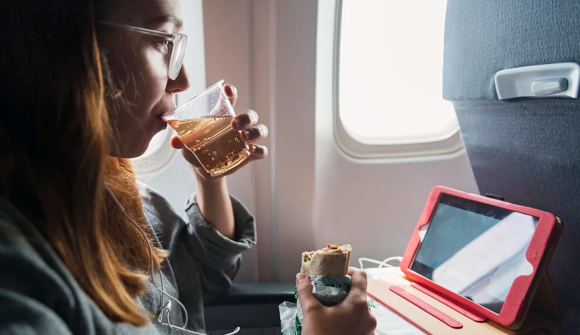 Millennial woman in comfy clothes travelling alone in plane. She is sitting comfortably, drinking ginger ale