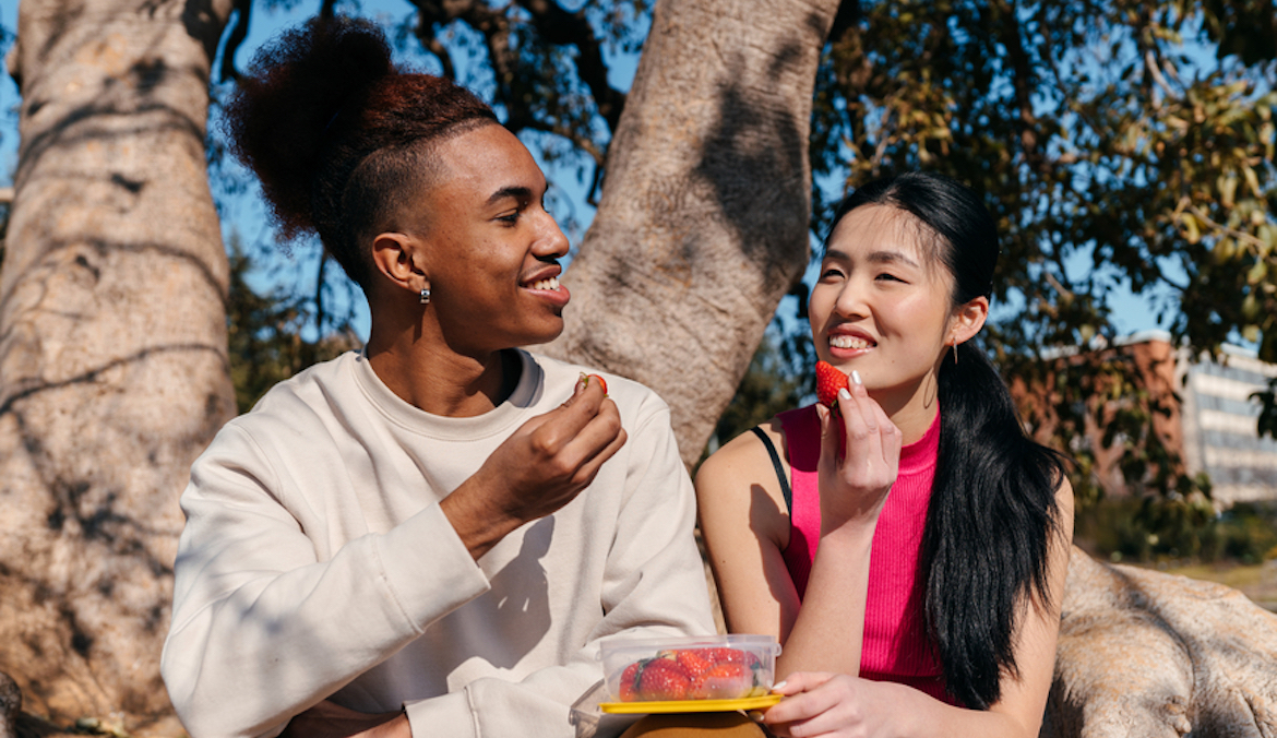 multiracial couple on a date sharing strawberries and talking outdoors in nature