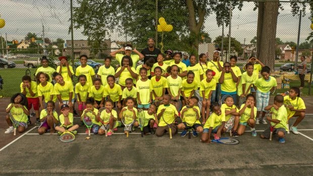 A classroom school picture style shot of the Palmer Park tennis academy students and teachers, showing around 30 kids, smiling and making funny faces, wearing neon yellow shirts with the Palmer Park logo.